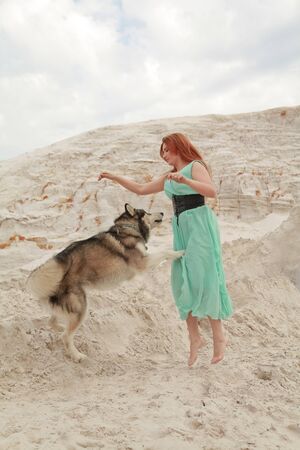 Funny best friends concept. Happy young female person walks in the desert with big dog malamute outdoorsの写真素材