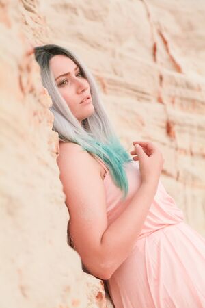 Young beautiful Caucasian woman in long pink dress posing in desert landscape with sand.の写真素材