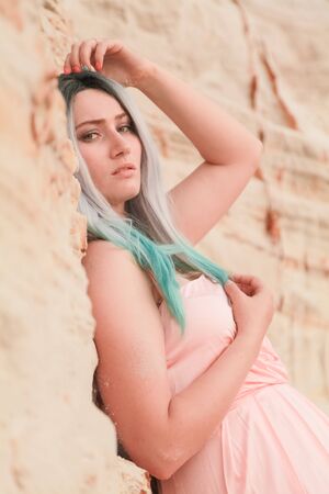 Young beautiful Caucasian woman in long pink dress posing in desert landscape with sand.の写真素材