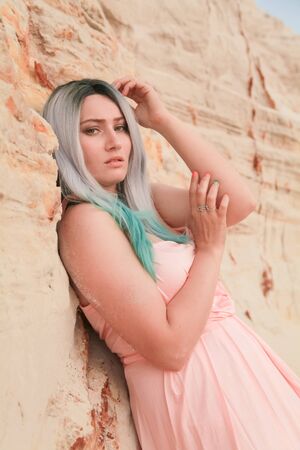 Young beautiful Caucasian woman in long pink dress posing in desert landscape with sand.の写真素材