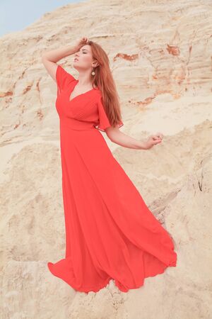 Young beautiful Caucasian woman in long bright outfit posing in desert landscape with sand.の写真素材
