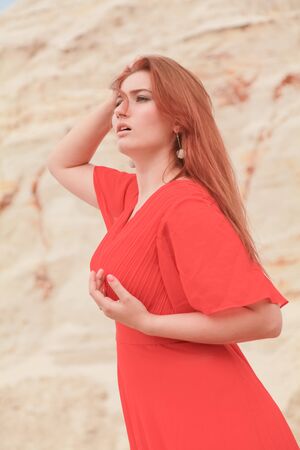 Young beautiful Caucasian woman in long bright outfit posing in desert landscape with sand.の写真素材