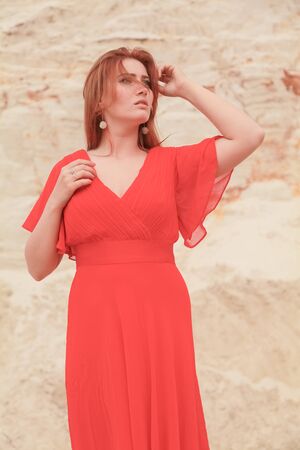 Young beautiful Caucasian woman in long bright outfit posing in desert landscape with sand.の写真素材