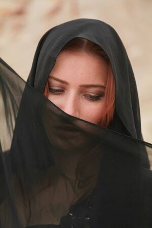 Young beautiful Caucasian woman in black chiffon dress posing in desert landscape with sand.の写真素材