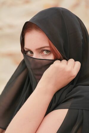 Young beautiful Caucasian woman in black chiffon dress posing in desert landscape with sand.の写真素材