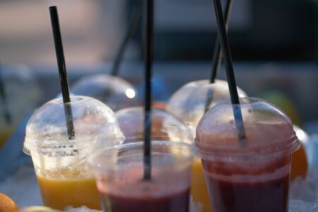 tasty frozen orange and red fresh juices in plastic cups in the sunの写真素材