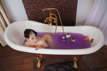 healthy naked goth girl with black hair in the luxury brown bathroom with purple salt waterの写真素材