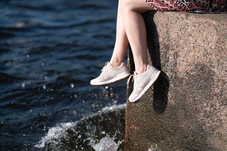 Womens legs sit on stone in the city and enjoy the summerの写真素材