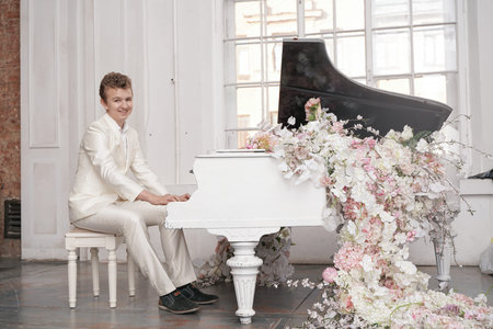 young teenager man with white big grand piano indoors alone enjoys musicの写真素材