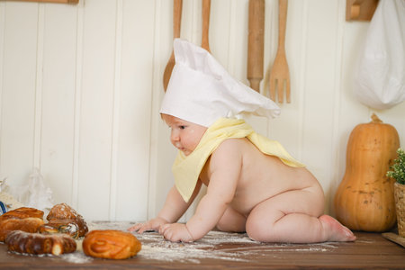 little baker child in chef hat at kitchen table alone