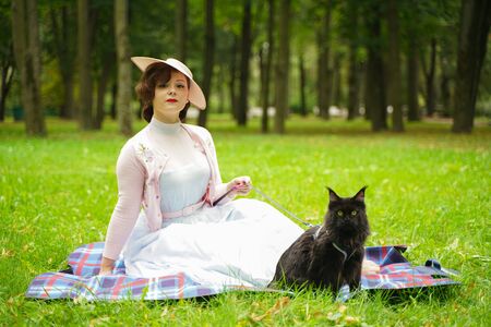 Pretty vintage woman walking with her black cat maine coon in the parkの写真素材
