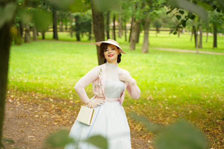 Portrait of pin up young woman in vintage dress and retro hat walking