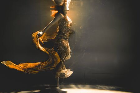 young woman swimming alone with fashion fabric underwater incognitoの写真素材
