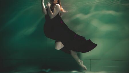 young woman swimming alone with fashion fabric underwater incognitoの写真素材