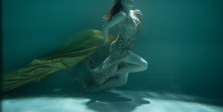 young woman swimming alone with fashion fabric underwater incognitoの写真素材