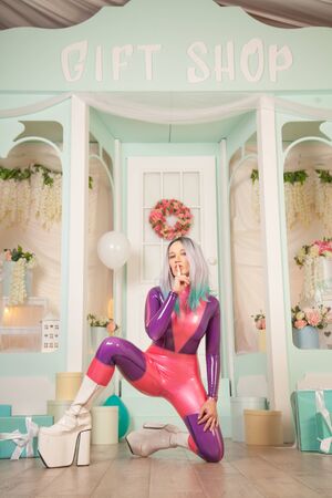 pretty cute adult girl in purple latex rubber costume posing near gift shop with presents and air balloons. fetish woman in tight outfit posing alone. full length portrait.の写真素材