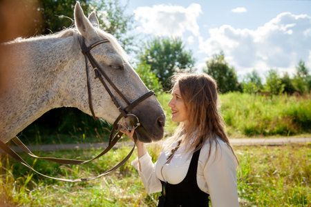 Beautiful caucasian young girl walking with a horse and enjoys summertime in countryside.