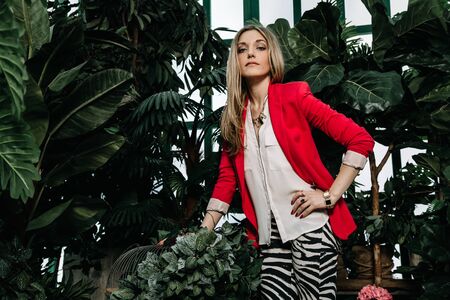 a young vegetarian woman owner poses in front of her greenhouse business with plants. the concept of tranquility among the city noise.の写真素材