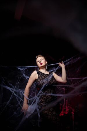 Woman in evening classic dress posing on black Halloween background with spider webの写真素材