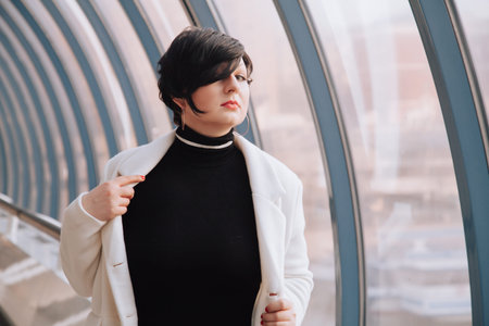Young beautiful stylish woman in white wool coat walking down the street. Plus size short hair adult...
