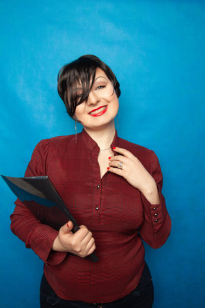 Portrait of happy woman in office, standing with folder on bluw studio background