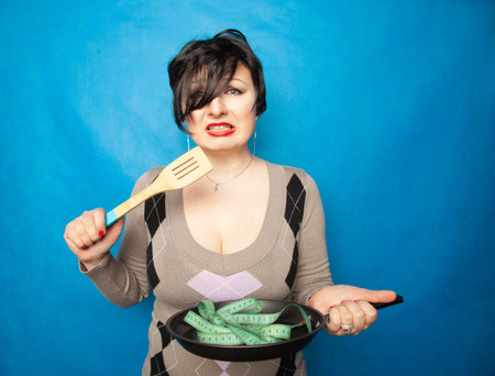 an emotional plus size girl with a short haircut stands in a sweater and holds an empty frying pan...