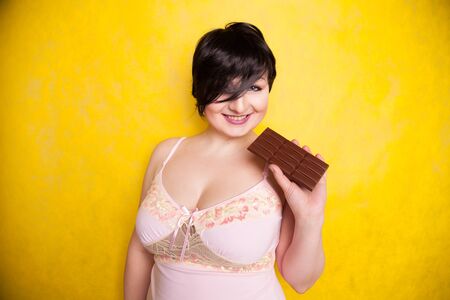 A beautiful plus-size woman flirts with taking a bite of dark chocolate.の写真素材