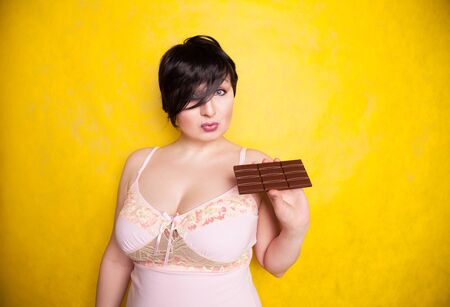 A beautiful plus-size woman flirts with taking a bite of dark chocolate.の写真素材