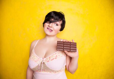 A beautiful plus-size woman flirts with taking a bite of dark chocolate.の写真素材