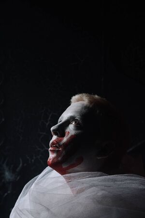 halloween make up. scary man ready for party. guy with a face covered in white paint and a bloody handprintの写真素材