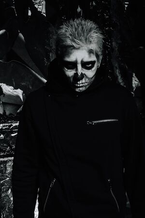 halloween make up. scary man ready for party. scary strange man with a painted skull on his face on black studio backgroundの写真素材