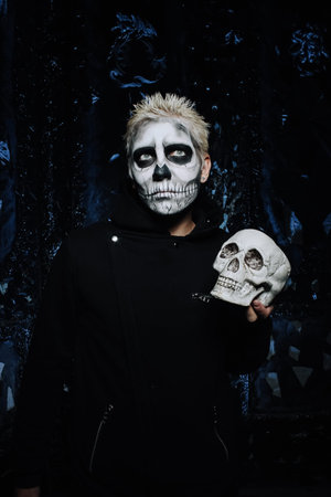 halloween make up. scary man ready for party. scary strange man with a painted skull on his face on black studio backgroundの写真素材