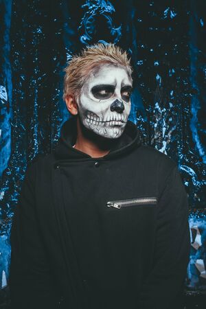 halloween make up. scary man ready for party. scary strange man with a painted skull on his face on black studio backgroundの写真素材