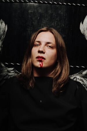 young long hair caucasian guy is going to go to a Halloween party in with makeup of blood from his mouthの写真素材