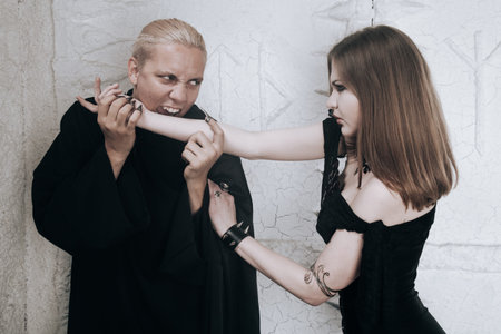 young vampire love couple in black halloween costumes ready for the party. man and woman bite and enjoy each other on white background.の写真素材