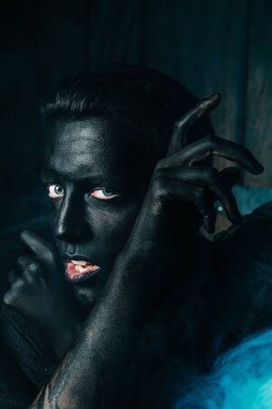 young caucasian man with white skin painted his face and hands to black color and love it. close up halloween portrait.の写真素材