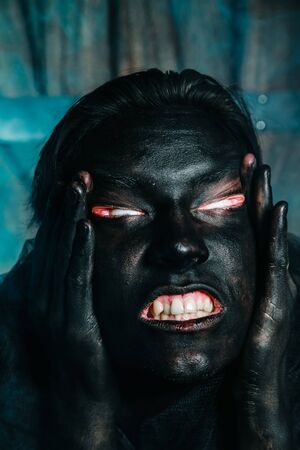 young caucasian man with white skin painted his face and hands to black color and love it. close up halloween portrait.の写真素材