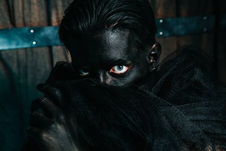 young caucasian man with white skin painted his face and hands to black color and love it. close up halloween portrait.の写真素材