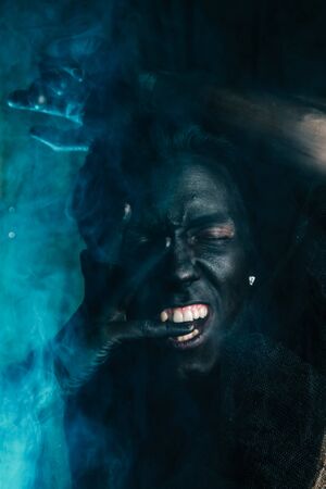 young caucasian man with white skin painted his face and hands to black color and love it. close up halloween portrait.の写真素材