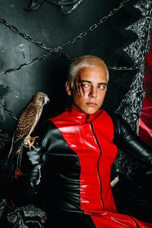 Gothic man with scary bloody makeup and bird of prey on huge scary throne ready for Halloween party