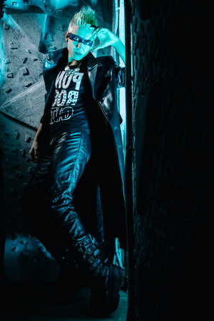 Fashion portrait of the young beautiful alternative man in leather long coat ready for party over...