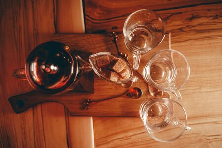 a Cup of clear glass tea, a small sugar bowl with a square of yellow sugar, and a teapot of tea on the wooden table.の写真素材