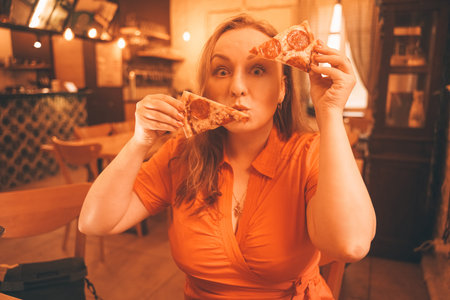 pretty plus size caucasian woman savoring and enjoying pizza in the pizzeriaの写真素材
