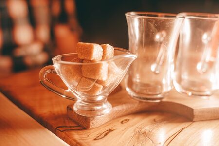 a Cup of clear glass tea, a small sugar bowl with a square of yellow sugar, and a teapot of tea on the wooden table.の写真素材