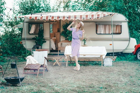 a cute woman with wavy blonde hair in a trendy summer striped dress on the background of a trailer...