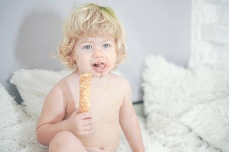 little child taking waffle and eating it with pleasure and fun on white room backgroundの写真素材