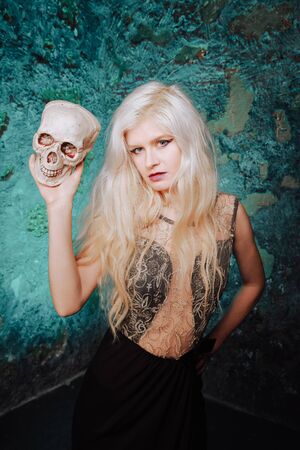 beautiful woman with blond hairstyle. adult slim girl with halloween skull in hands. mystic light.の写真素材