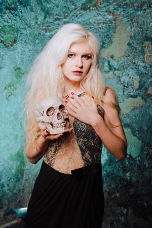 beautiful woman with blond hairstyle. adult slim girl with halloween skull in hands. mystic light.の写真素材