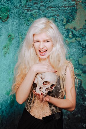 beautiful woman with blond hairstyle. adult slim girl with halloween skull in hands. mystic light.の写真素材