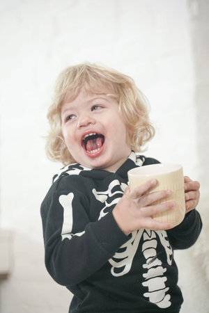 Beautiful little boy enjoying a cup of drink at white home background